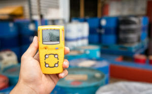 Gelbes Pruefgas Gaswarnmessgeraet in Hand prüft Messwerte vor Faessern mit Chemikalien